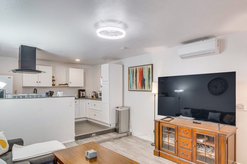 Gallery – The Surf Retreat 1 Bright and modern open-concept living room and kitchen space with cozy gray sectional, flat-screen TV, and fully equipped white kitchen – perfect for long-term or short-term rentals, sober living homes, and military housing.